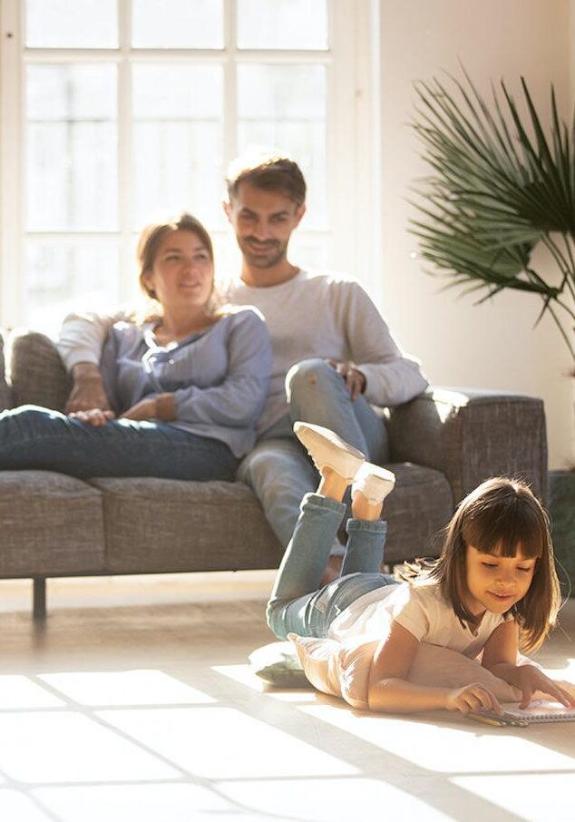 Happy parents relaxing on couch while kid drawing on floor